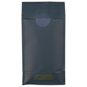 The back of a navy blue recyclable bag containing 1kg of specialty coffee beans. It says in gold 'Purchase beans or start a subscription at patriciacoffee.com.au'. There is also a round embossed sticker with Patricia opening date of 15 of December, 2011.