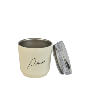 A cream coloured Kinto 240ml reusable coffee tumbler, with the lid off to the side, leaning on the cup. The Patricia logo printed in black on the front of it.