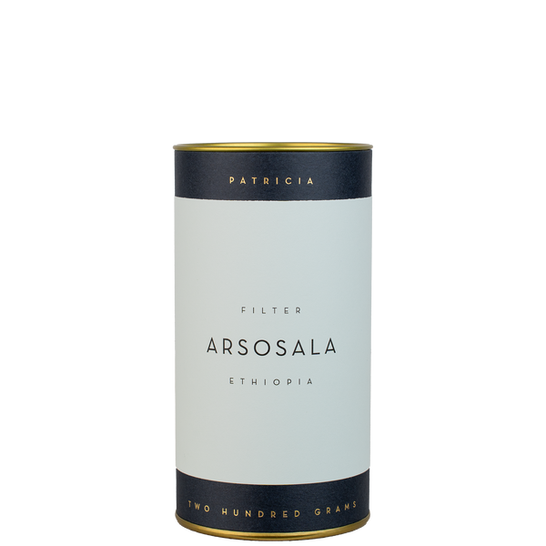 A navy blue cylinder with a light blue label describes the roasted coffee beans within. 'PATRICIA' and 'TWO HUNDRED GRAMS' are printed in gold foil.