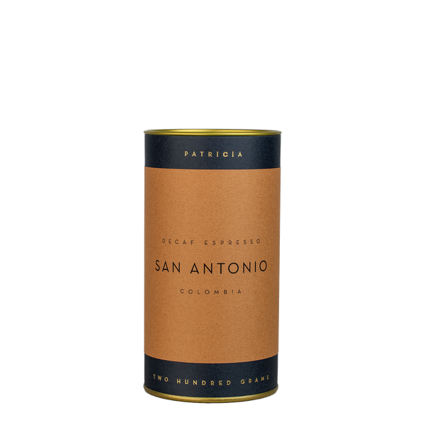 A navy blue cylinder with a brown label describes the roasted decaf coffee beans within. 'PATRICIA' and 'TWO HUNDRED GRAMS' are printed in gold foil.