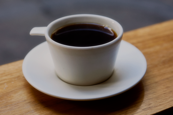 A batch brewed filter coffee in a ceramic cup made by Malcolm Greeenwood, with a paddle instead of a traditional handle. It sits on the wooden windowsill of Patricia.
