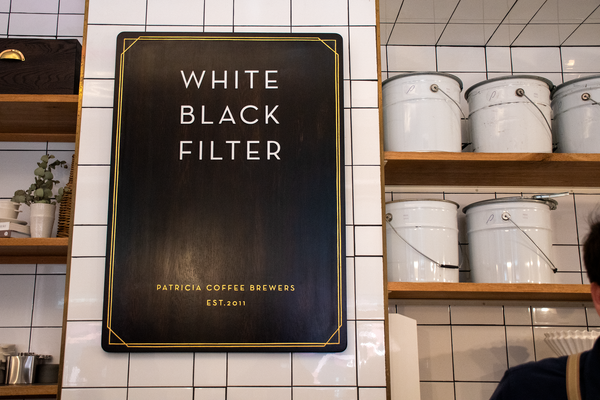 Patricia's giant wooden cafe menu displaying the words 'White, Black, Filter' stacked on top of each other, as well as 'Patricia Coffee Brewers, EST. 2011' in gold paint.