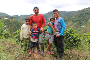 Contributing producer Neyid Pillimué Sr. and his family at his farm El Carmen. They stand smiling in front of coffee trees on the edge of a green valley.