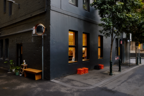 Patricia Coffee Brewers, viewed from outside. There are milk crates arranged outside on the slightly damp ground, as well as plants and some retail coffee beans on a small step ladder. A warm light emits from within.