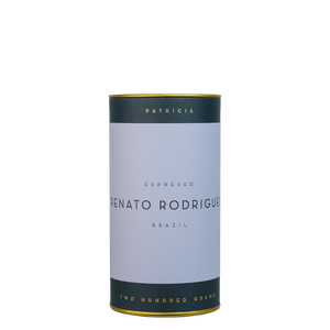 A navy blue cylinder with a light purple label describes the roasted coffee beans within. 'PATRICIA' and 'TWO HUNDRED GRAMS' are printed in gold foil.