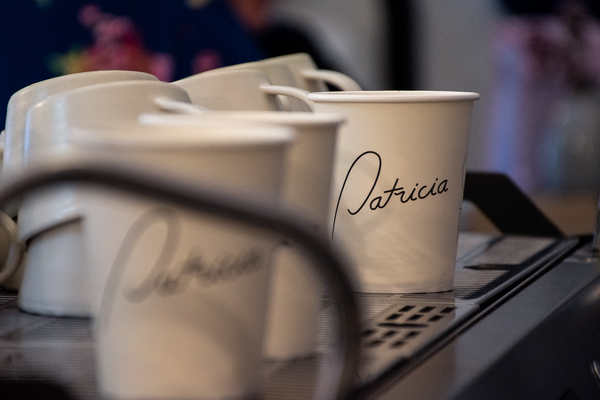 Three takeaway cups with Patricia's logo sit atop a La Marzocco Strada espresso machine, waiting to be filled with delicious coffee.