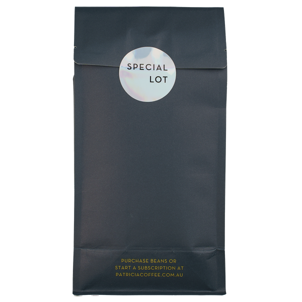The back of a navy blue recyclable bag containing 1kg of specialty coffee beans. It says in gold 'Purchase beans or start a subscription at patriciacoffee.com.au'. There is also a shiny round sticker that says 'SPECIAL LOT'
