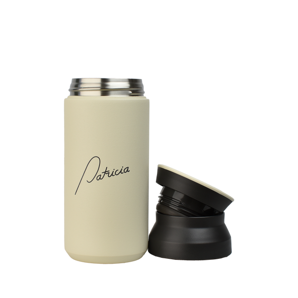 A cream coloured Kinto 350ml Tumbler with the Patricia logo printed in black on the front. The two-part lid has been removed and is sitting next to it.