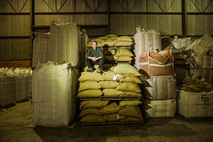 Fabiano Borré sit's smiling, atop green coffee sacks in a warehouse.