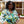 Lucy Wanja Ndogo smiling and wearing a colourful shirt, in front of the Rurima homestead.
