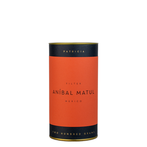 A navy blue cylinder with an red label describes the roasted coffee beans within. 'PATRICIA' and 'TWO HUNDRED GRAMS' are printed in gold foil.