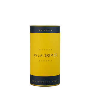 A navy blue cylinder with a yellow label describes the roasted coffee beans within. 'PATRICIA' and 'TWO HUNDRED GRAMS' are printed in gold foil.
