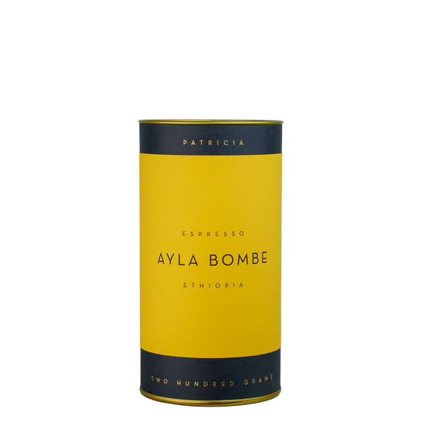 A navy blue cylinder with a yellow label describes the roasted coffee beans within. 'PATRICIA' and 'TWO HUNDRED GRAMS' are printed in gold foil.