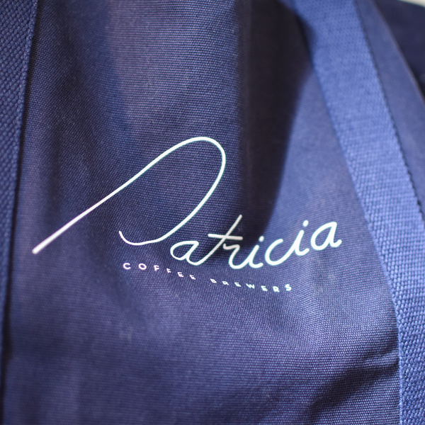 Close up of the Patricia logo printed in white on a navy blue tote bag in the sunlight.