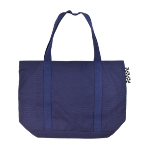 The back of the Patricia navy blue tote bag. A black and white tag in the floor tile pattern of the cafe is visible on the right side.