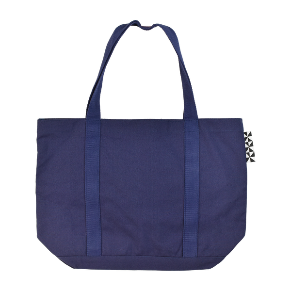 The back of the Patricia navy blue tote bag. A black and white tag in the floor tile pattern of the cafe is visible on the right side.