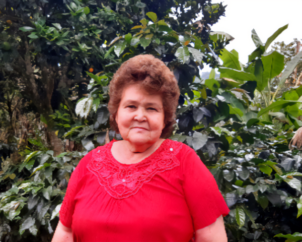 Blanca Lopez stands in front of her lush coffee trees wearing a red blouse.