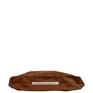 The bottom of a brown canvas tote bag with a white label reading 'A FRIENDLY PLACE FOR COFFEE'.