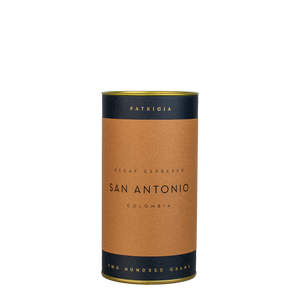 A navy blue cylinder with a brown label describes the roasted decaf coffee beans within. 'PATRICIA' and 'TWO HUNDRED GRAMS' are printed in gold foil.