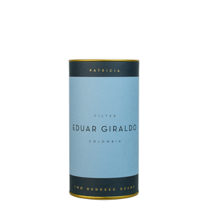 A navy blue cylinder with a blue label describes the roasted coffee beans within. 'PATRICIA' and 'TWO HUNDRED GRAMS' are printed in gold foil.