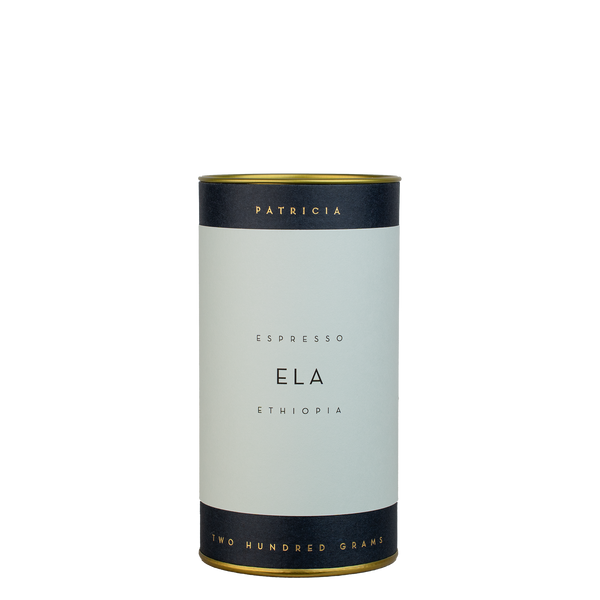 A navy blue cylinder with a light blue label describes the roasted coffee beans within. 'PATRICIA' and 'TWO HUNDRED GRAMS' are printed in gold foil.
