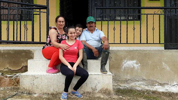 Faver, Andrea and their children sit on steps outside their colourful house.