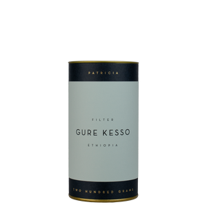 A navy blue cylinder with a light blue label describes the filter coffee beans within. 'PATRICIA' and 'TWO HUNDRED GRAMS' are printed in gold foil.