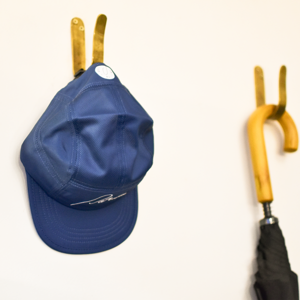 A blue running cap hangs on a brass hook on the wall at Patricia Coffee Brewers. Next to it is a wooden handled umbrella.