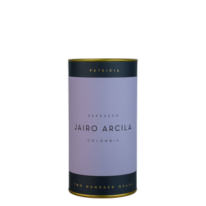 A navy blue cylinder with a purple label describes the roasted coffee beans within. 'PATRICIA' and 'TWO HUNDRED GRAMS' are printed in gold foil.