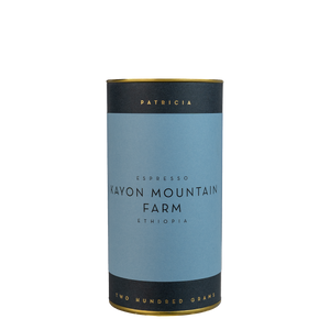 A navy blue cylinder with a blue label describes the espresso coffee beans within. 'PATRICIA' and 'TWO HUNDRED GRAMS' are printed in gold foil.