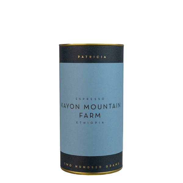 A navy blue cylinder with a blue label describes the espresso coffee beans within. 'PATRICIA' and 'TWO HUNDRED GRAMS' are printed in gold foil.