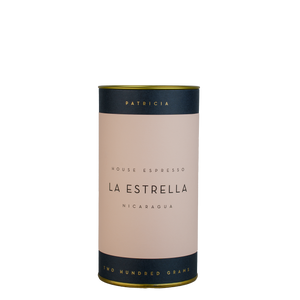 A navy blue cylinder with a pink label describes the espresso coffee beans within. 'PATRICIA' and 'TWO HUNDRED GRAMS' are printed in gold foil.