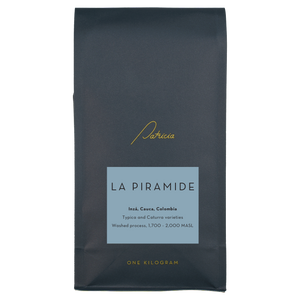 A navy blue recyclable bag containing 1kg of specialty coffee beans. It has the Patricia logo in gold, the coffee's name on a blue sticker, and 'One kilogram' in gold underneath.