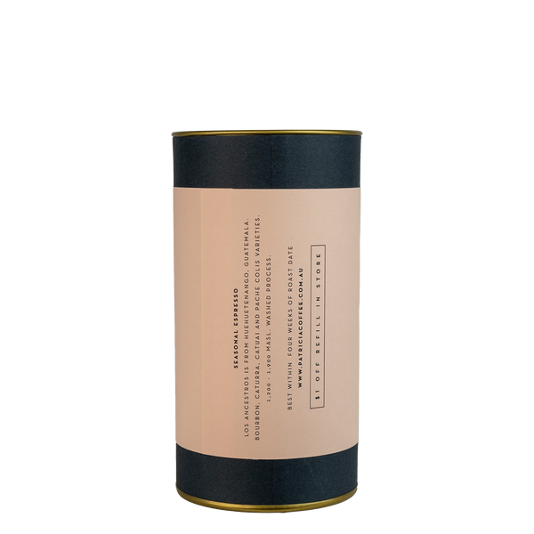 A navy blue cylinder with a pink label describes the espresso coffee beans within.