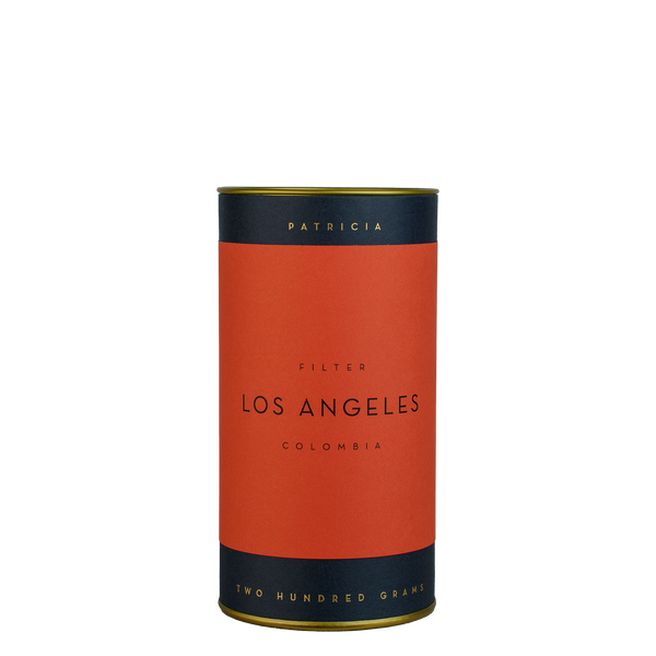 A navy blue cylinder with a red label describes the roasted coffee beans within. 'PATRICIA' and 'TWO HUNDRED GRAMS' are printed in gold foil.