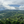 Green hills and valleys under a cloudy sky with coffee trees in the foreground