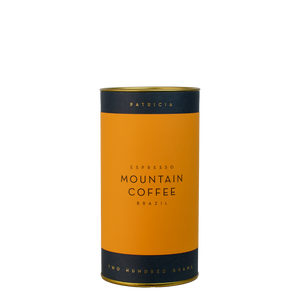 A navy blue cylinder with an orange label describes the roasted coffee beans within. 'PATRICIA' and 'TWO HUNDRED GRAMS' are printed in gold foil.