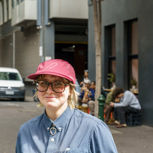 Person wearing a red running cap with a pink P on the front, outside Patricia Coffee Brewers