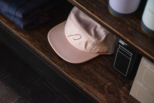 A light pink running cap with the Patricia 'P' embroidered in maroon on the front panel, and Fractel on the left panel, sits on the shelf at Patricia Coffee Brewers.