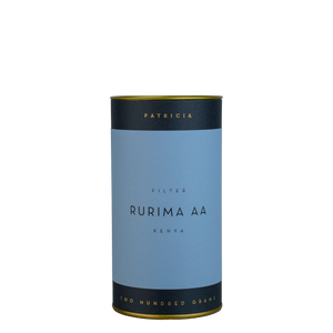 A navy blue cylinder with a blue label describes the roasted coffee beans within. 'PATRICIA' and 'TWO HUNDRED GRAMS' are printed in gold foil.