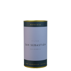 A navy blue cylinder with a violet label describes the roasted coffee beans within. 'PATRICIA' and 'TWO HUNDRED GRAMS' are printed in gold foil.