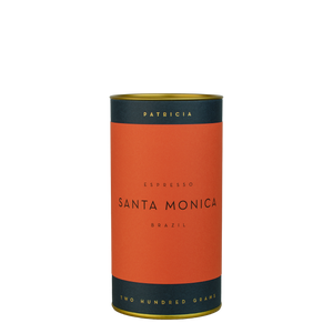 A navy blue cylinder with a red label describes the roasted coffee beans within. 'PATRICIA' and 'TWO HUNDRED GRAMS' are printed in gold foil.