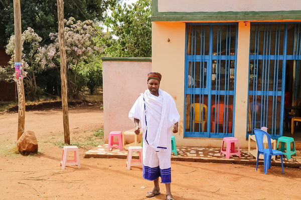 Ture Waji stands outside a building with colourful plastic stools surrounding him.